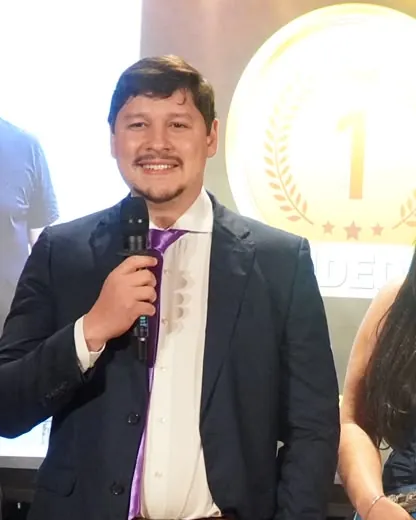 Caio Vinícius no palco de uma premiação, com uma medalha de primeiro lugar no telão